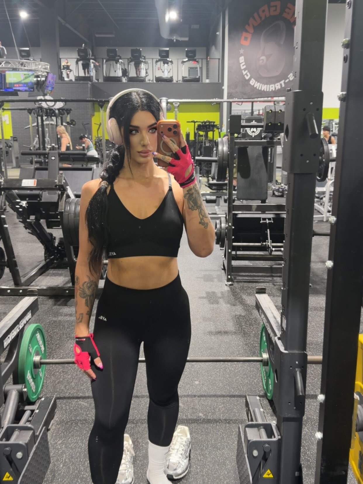 Ally on the gym floor in black activewear with pink workout gloves and headphones